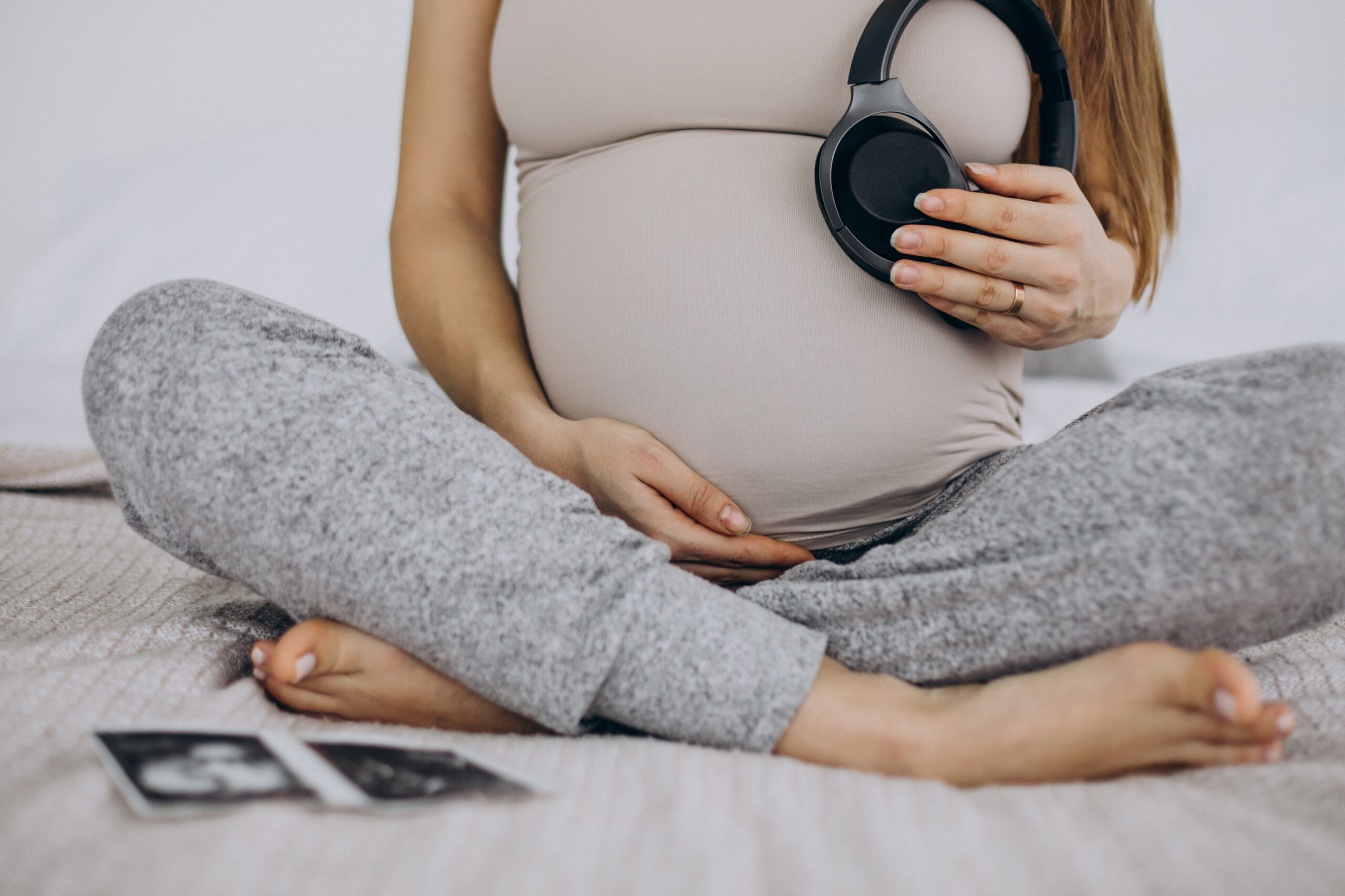 Pregnant woman with ultrasound photo putting headphones with music on her belly